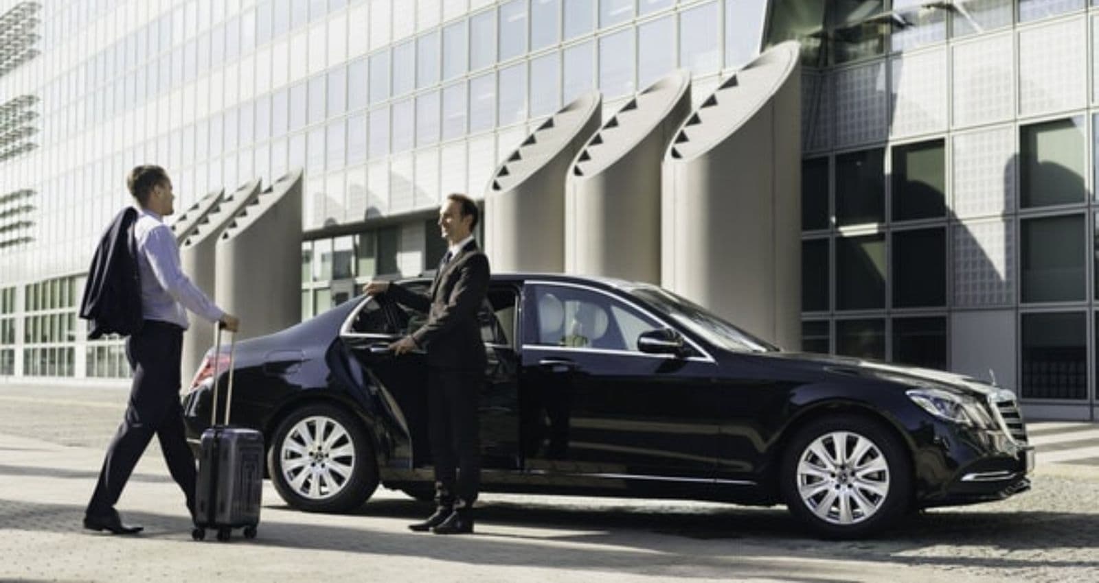 man opening door of mercedes car for another man with luggage